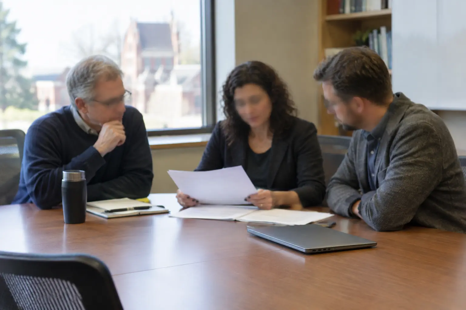 A small academic committee reviewing a final thesis document together at a conference table